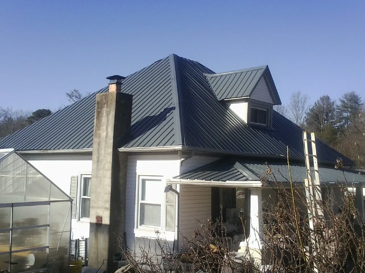 Dark blue standing seam metal roof on a white farmhouse with dormer — Slate & Tile Roof Repair by Roofing Brothers in Hooper