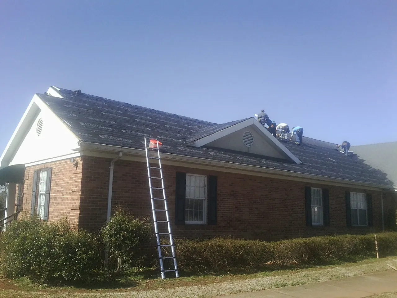 Crew tearing shingles off a brick ranch roof with a ladder set — Metal Roof Repair work by our crew in Hooper