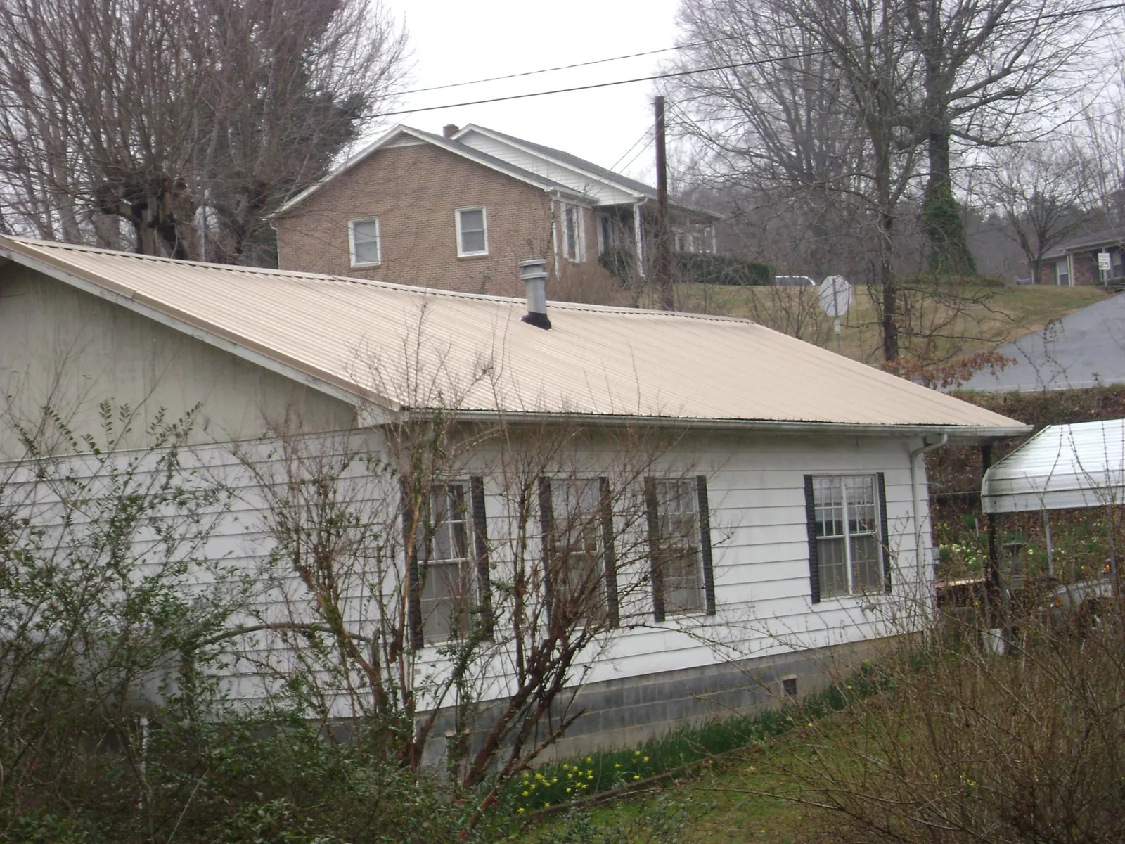 Tan metal roof on a white sided house set into a hillside — Commercial Roofing by Roofing Brothers in Hooper